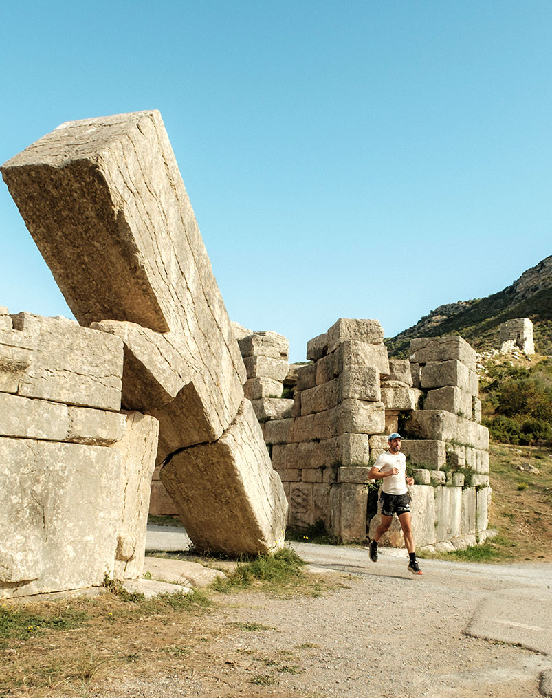 Runners on coastal rocks by a lighthouse in Greece